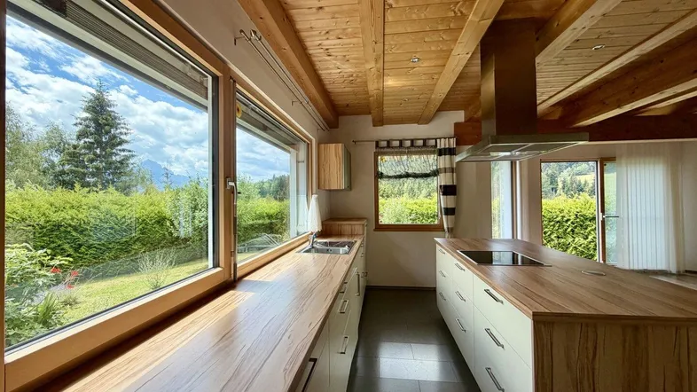 Helle Küche mit Holzbalkendecke, großen Fenstern und Blick ins Grüne.