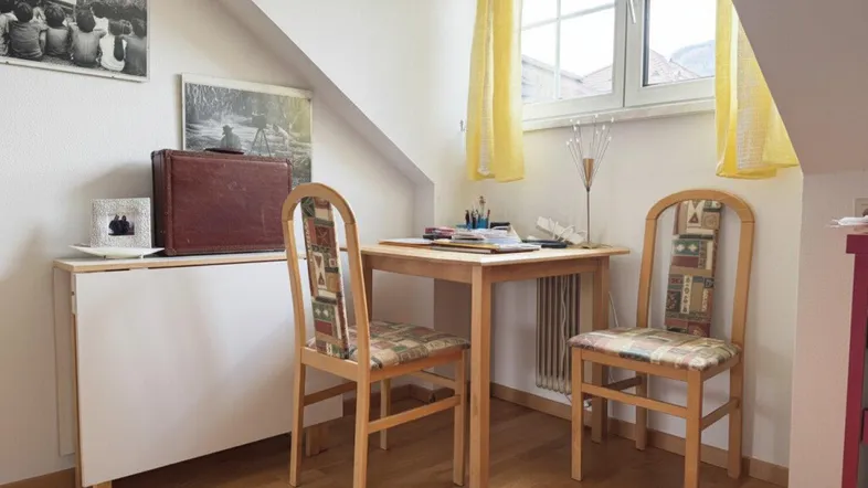 Kleiner Arbeitsbereich unter der Dachschräge mit Holzboden und Fenster mit gelben Vorhängen.