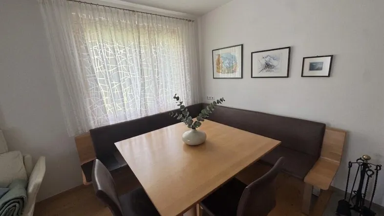 Gemütlicher Essbereich mit Holztisch, Eckbank und hellem Vorhang, ideal für Familienmahlzeiten.