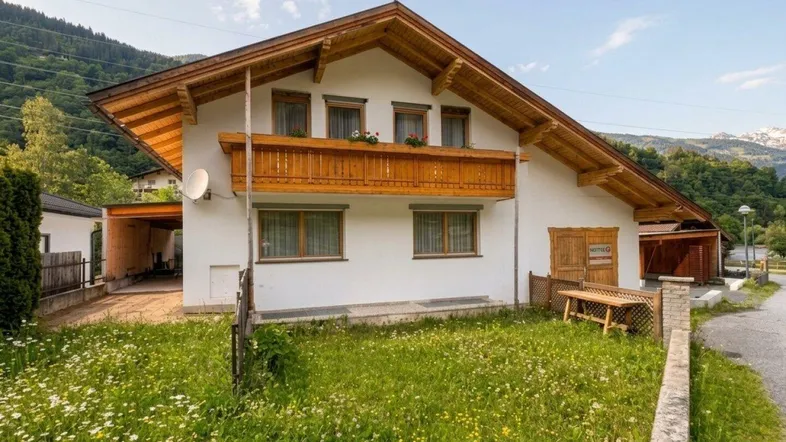 Traditionelles Haus im alpinen Stil mit Holzbalkon und Blick auf die umliegende Berglandschaft.