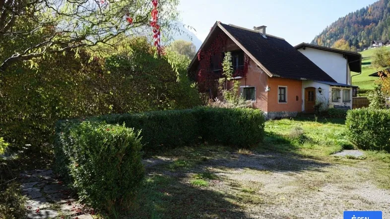 Charmantes Haus mit gepflegtem Garten, umgeben von grünen Hecken und Bergblick.