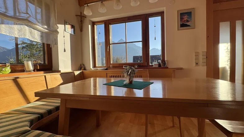 Heller Essbereich mit Holztisch, eingebauter Sitzbank und weitem Bergblick durch große Fenster.
