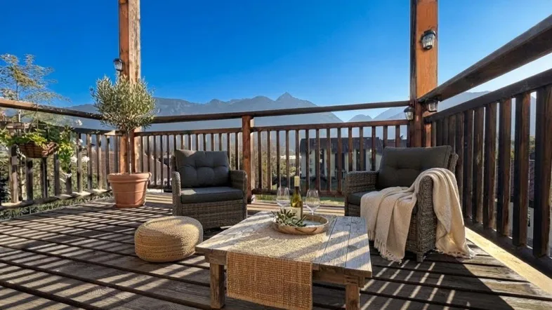 Geräumiger Holzbalkon mit gemütlichen Sitzgelegenheiten und weitem Blick auf die Berge.