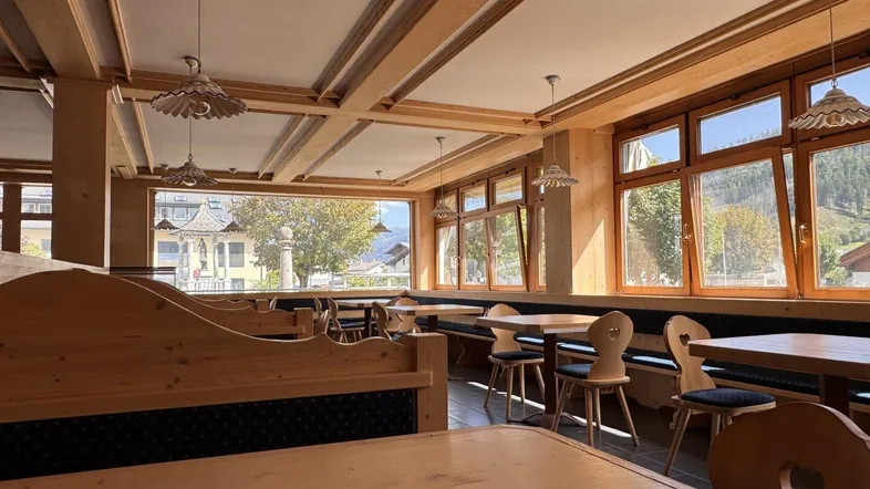 Geräumiger Speisesaal mit traditionellen Holzmöbeln, großen Fenstern und Blick auf die Berge.