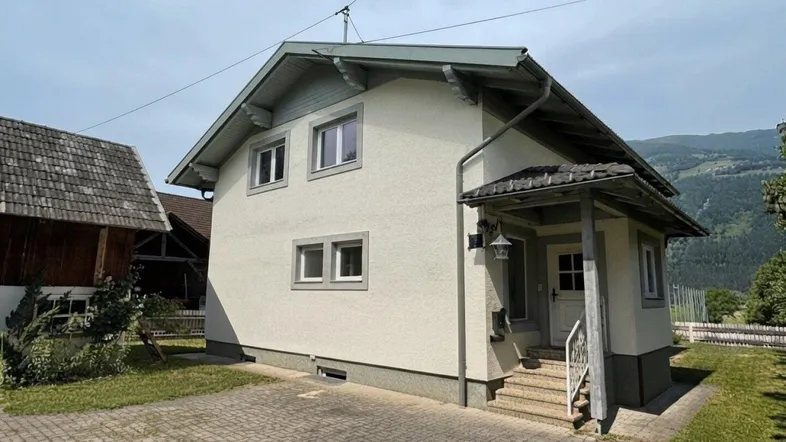 Ansicht des Hauses von vorne mit gepflasterter Einfahrt, überdachtem Eingang und Bergblick.
