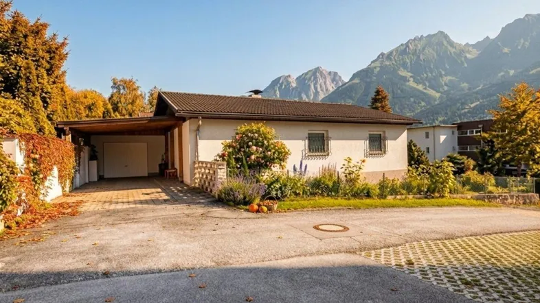Einfamilienhaus mit Carport und Einfahrt, umgeben von Bäumen und Bergen im Hintergrund.