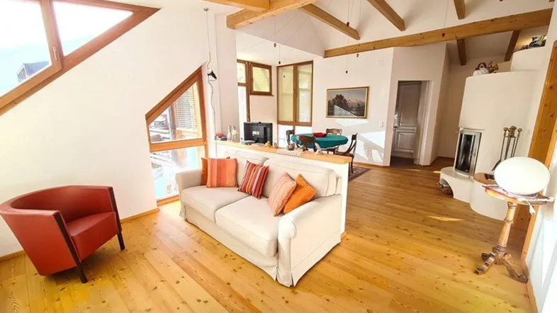 Helles Wohn- und Esszimmer mit Holzbalken, großen Fenstern, Kamin und rustikalem Holzdielenboden.