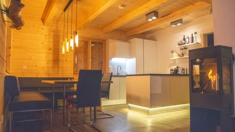 Gemütlicher Wohn-Essbereich mit Holzbalkendecke, moderner Küche und Kaminofen.