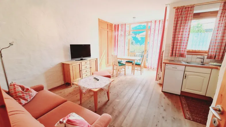 Helles Wohnzimmer mit integrierter Küchenzeile, Esstisch und Zugang zum Balkon.