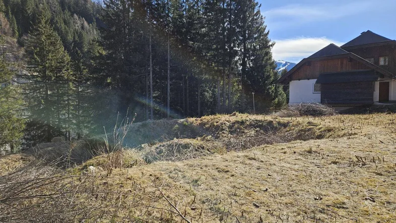 Weitläufiges Grundstück in alpiner Umgebung mit altem Gebäude und Bergblick.