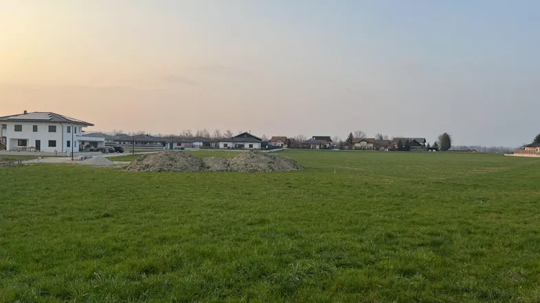 Weitläufiges grünes Feld mit Blick auf umliegende Wohnhäuser und Bauland unter klarem Himmel.