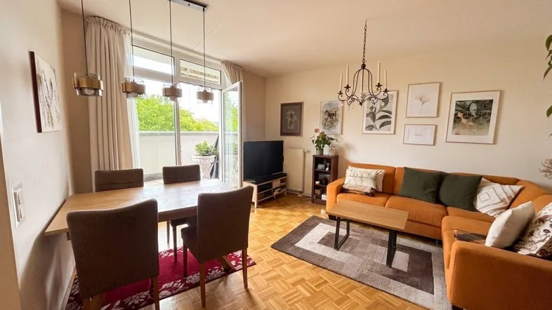 Helles Wohn-Esszimmer mit Parkettboden, gemütlicher Sitzecke und Zugang zum Balkon.