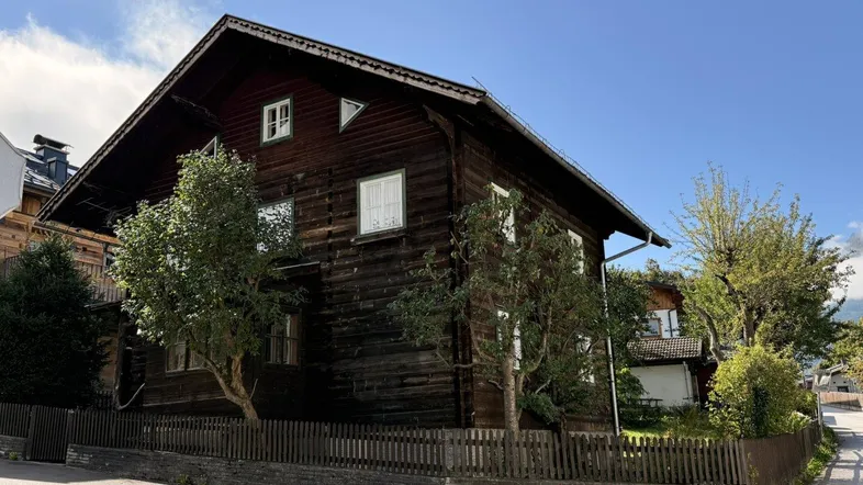 Traditionelles Holzhaus mit Satteldach und Holzzaun unter blauem Himmel.