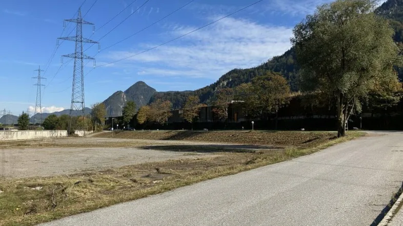 Weitläufiges Grundstück mit Schotterfläche und Blick auf die umliegenden Berge und Strommasten unter blauem Himmel.