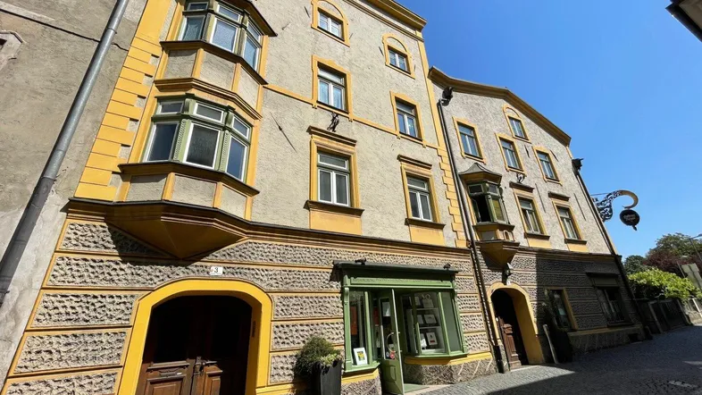 Historisches Gebäude mit markanter gelb-grauer Fassade, Erkern und traditioneller Architektur an einer Kopfsteinpflasterstraße.