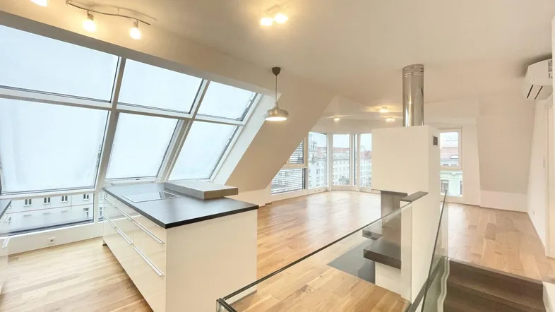 Helles Dachgeschoss-Apartment mit offener Küche, Holzboden und großen Fenstern, die viel Tageslicht hereinlassen.