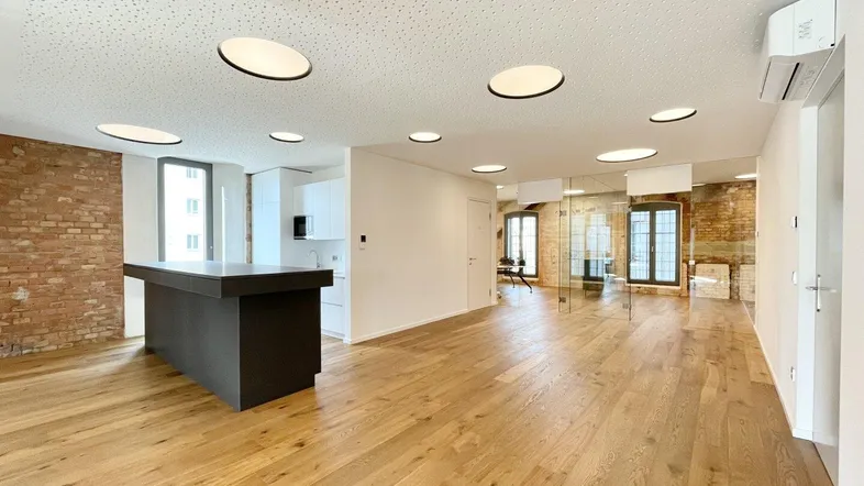 Geräumiger offener Bürobereich mit moderner Küchenzeile, Holzboden und freiliegenden Ziegelwänden, hell und einladend.