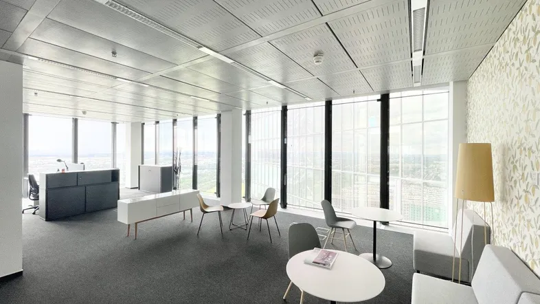Moderner Büroraum mit Teppichboden, großen Fenstern und einer gemütlichen Sitzecke mit Blick auf die Stadt.
