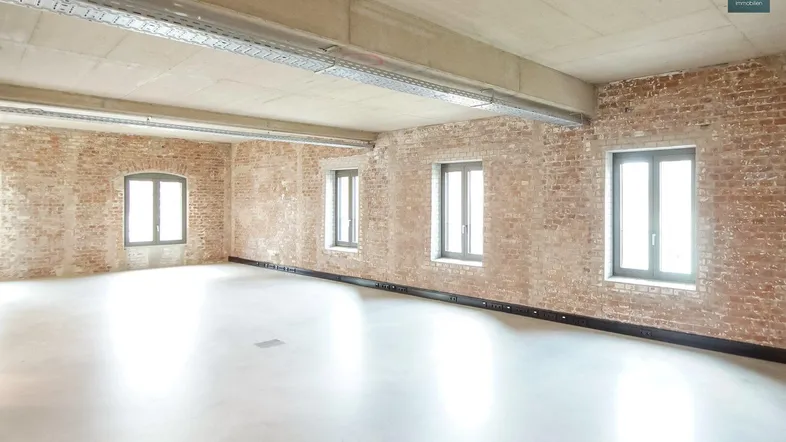 Großer, heller Büroraum mit unverputzten Ziegelwänden und Sichtbetondecke, bereit zur individuellen Gestaltung.