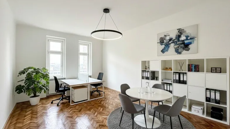 Geräumiges Büro mit Fischgrätparkett, zwei Arbeitsplätzen und einem Besprechungsbereich mit runden Tisch.