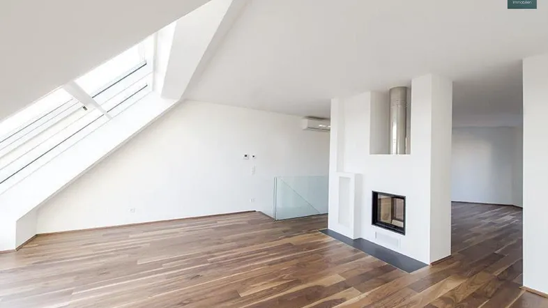 Helles Dachgeschoss-Wohnzimmer mit Holzboden, Kamin und großen Dachfenstern.