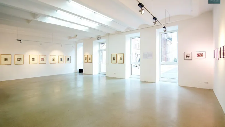 Heller, offener Gewerberaum mit hohen Decken, Betonboden und großen Fenstern, aktuell als Galerie genutzt.