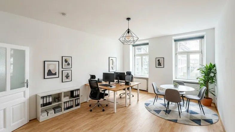 Geräumiges Büro mit Holzboden, zwei Arbeitsplätzen, einem Besprechungstisch und viel Tageslicht.