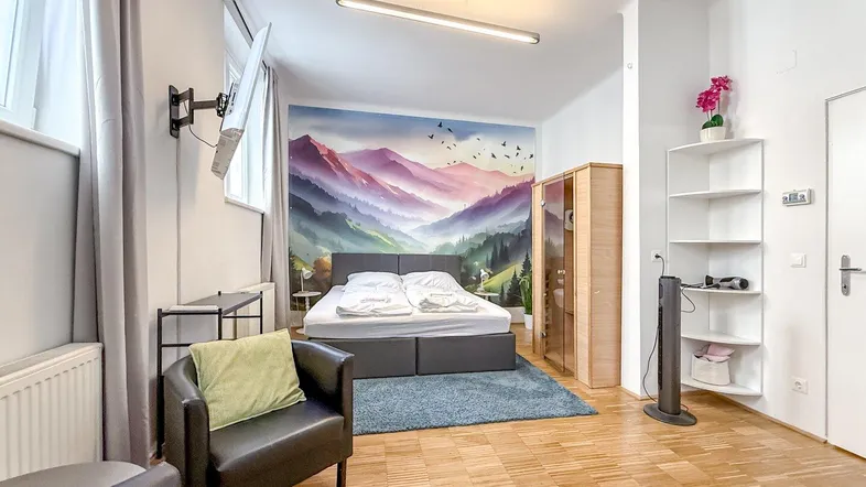 Helles Schlafzimmer mit Doppelbett, Parkettboden und dekorativer Wandtapete mit Bergmotiv.