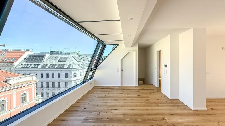 Heller, moderner Raum mit Holzboden und großen, schrägen Fenstern mit Stadtblick.