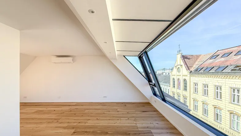 Helles Zimmer mit Holzboden, Dachschrägen und großen Fenstern mit Stadtblick.