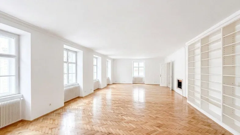 Großzügiges, helles Wohnzimmer mit Fischgrätparkett, hohen Fenstern und integriertem Bücherregal mit Kamin.
