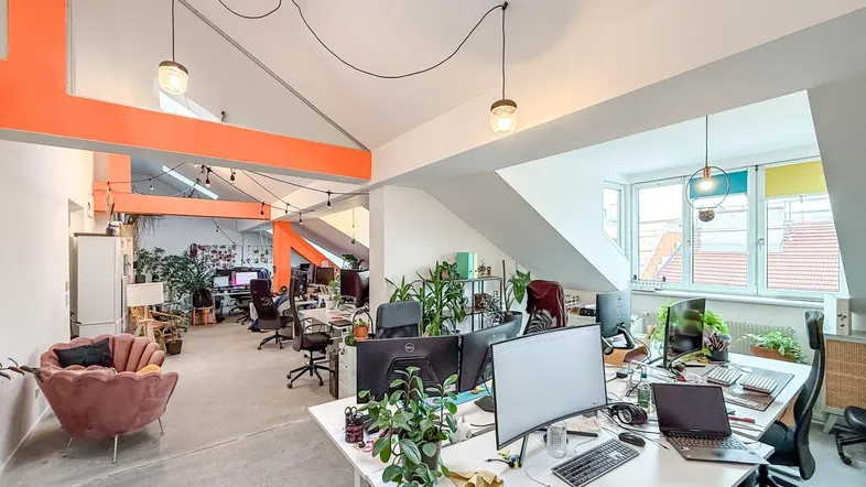 Großzügliches Großraumbüro mit modernen Arbeitsplätzen, vielen Pflanzen und hellen Dachfenstern.