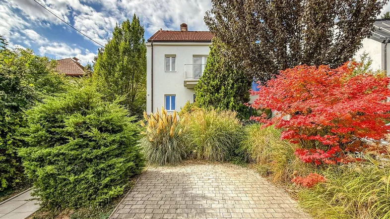 Gepflasterte Einfahrt vor dem weißen Wohnhaus mit üppiger Bepflanzung und Herbstfarben.