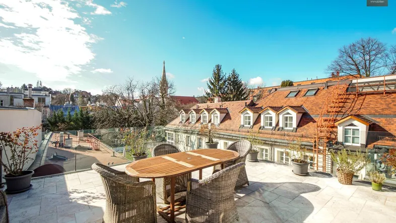 Geräumige Dachterrasse mit Korbmöbeln und weitem Blick über die Dächer der Stadt.