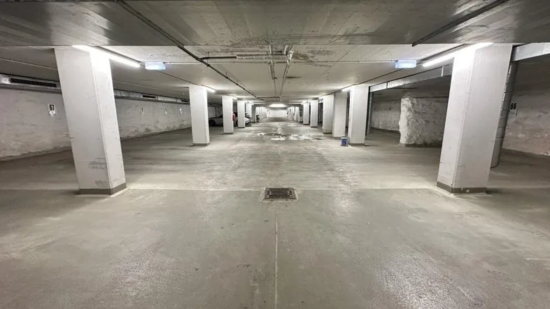Lange Tiefgarage mit Betonboden und Säulen, gut beleuchtet durch Deckenleuchten.