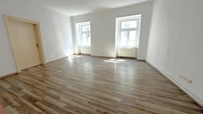 Heller, leerer Raum mit Laminatboden und zwei Fenstern, ideal als Wohnzimmer nutzbar.