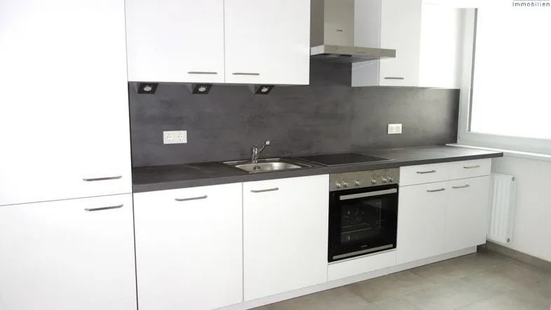 Moderne Küche mit weißen Hochglanzfronten, dunkler Arbeitsplatte und integrierten Geräten.