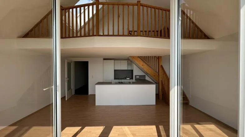 Heller offener Wohnbereich mit moderner Küche, Holzparkett und Galerie, durch große Glastüren zur Terrasse.