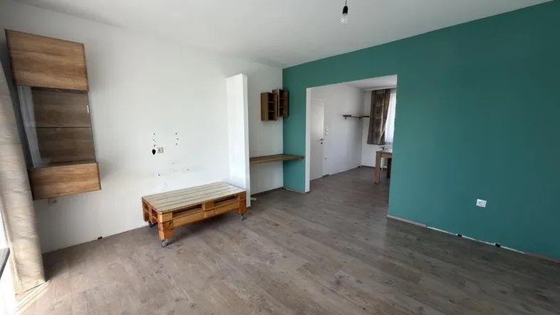 Helles Wohnzimmer mit Laminatboden, einer grünen Akzentwand und einfacher Einrichtung.