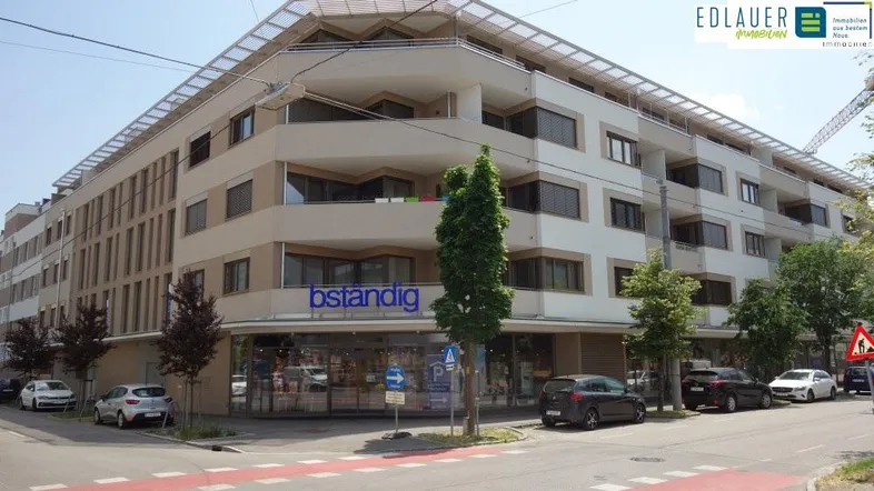 Modernes Mehrfamilienhaus mit Geschäften im Erdgeschoss und Balkonen in urbaner Umgebung.