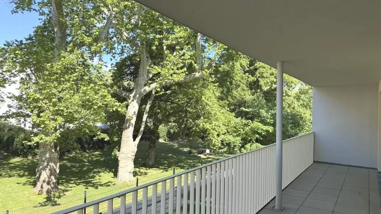 Geräumiger Balkon mit Fliesenboden und einem schönen Blick ins Grüne mit alten Bäumen.