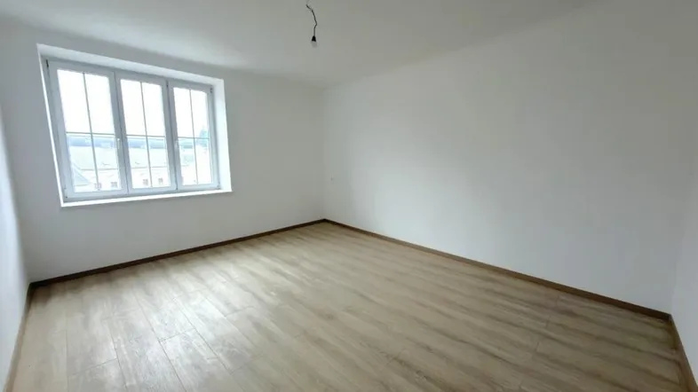 Helles, leeres Zimmer mit Laminatboden und großen Fenstern, bereit zur individuellen Gestaltung.