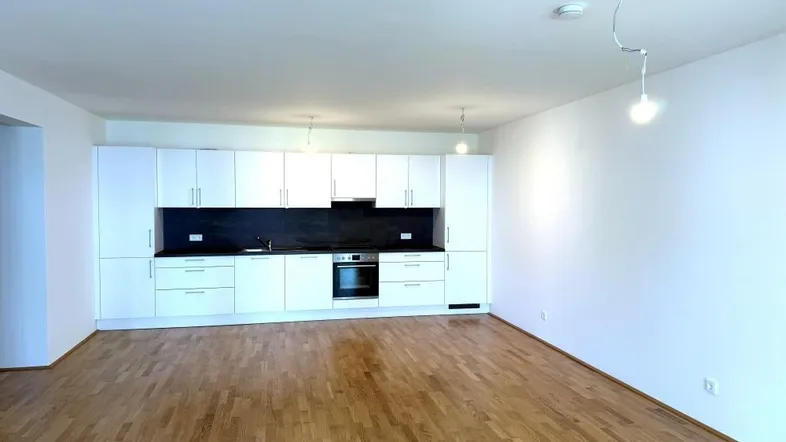 Moderne, weiße Einbauküche mit dunkler Arbeitsplatte und integriertem Backofen in einem offenen Wohnbereich mit hellem Holzparkett.