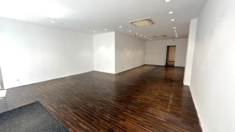 Geräumiger, leerer Geschäftsraum mit dunklem Holzfußboden, weißen Wänden und integrierter Deckenbeleuchtung.