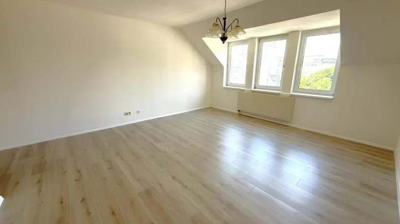 Helles Zimmer mit Dachschräge, Laminatboden und drei Fenstern, ideal als Wohn- oder Schlafzimmer.