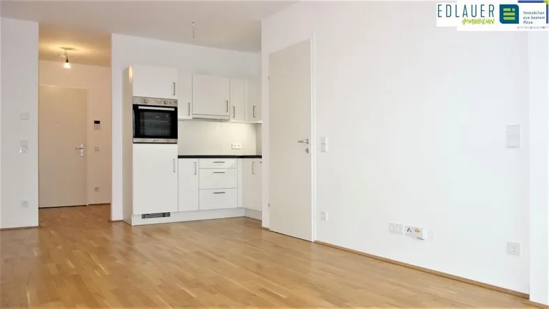 Heller Wohn- und Kochbereich mit Parkettboden und integrierter Küchenzeile in modernem Design.