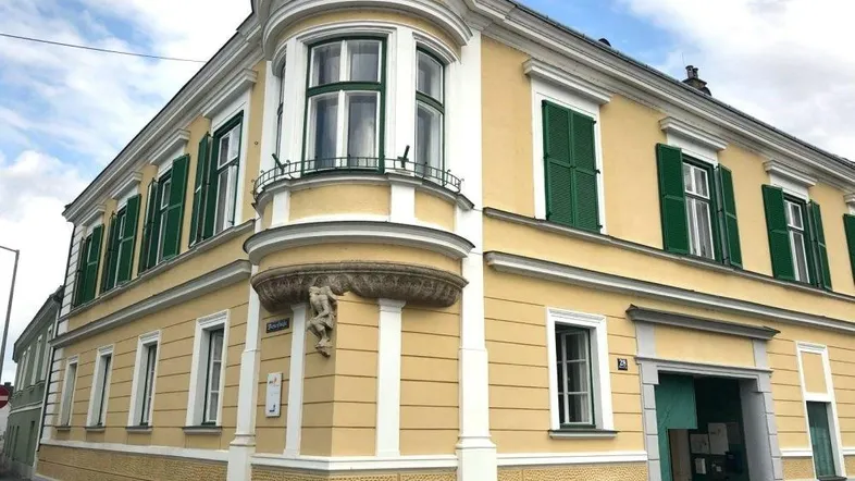 Historisches Eckgebäude mit gelber Fassade, grünen Fensterläden und einem markanten Erker.