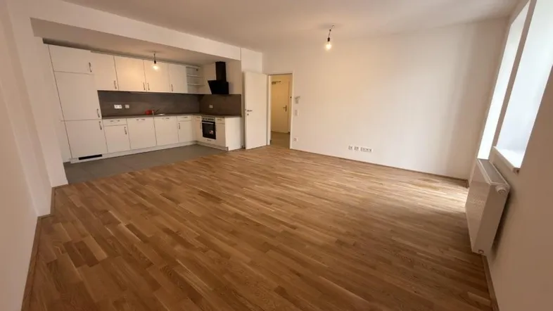 Helles Wohnzimmer mit offener Küche, Parkettboden und weißen Schränken.
