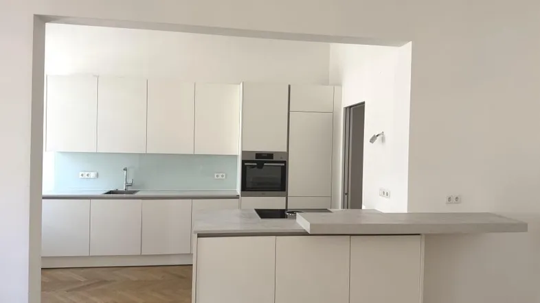 Helle, moderne Küche mit weißen Fronten, Kücheninsel und integriertem Backofen.
