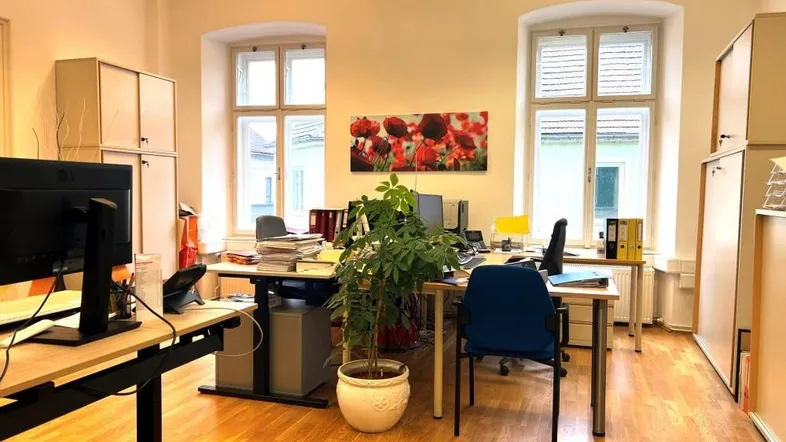 Geräumiges Büro mit mehreren Arbeitsplätzen, großen Fenstern und Holzboden, das viel Tageslicht erhält.